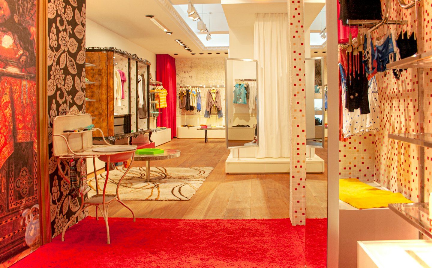 Boutique di abbigliamento colorata con merce su scaffali e un tavolino da toeletta decorativo.