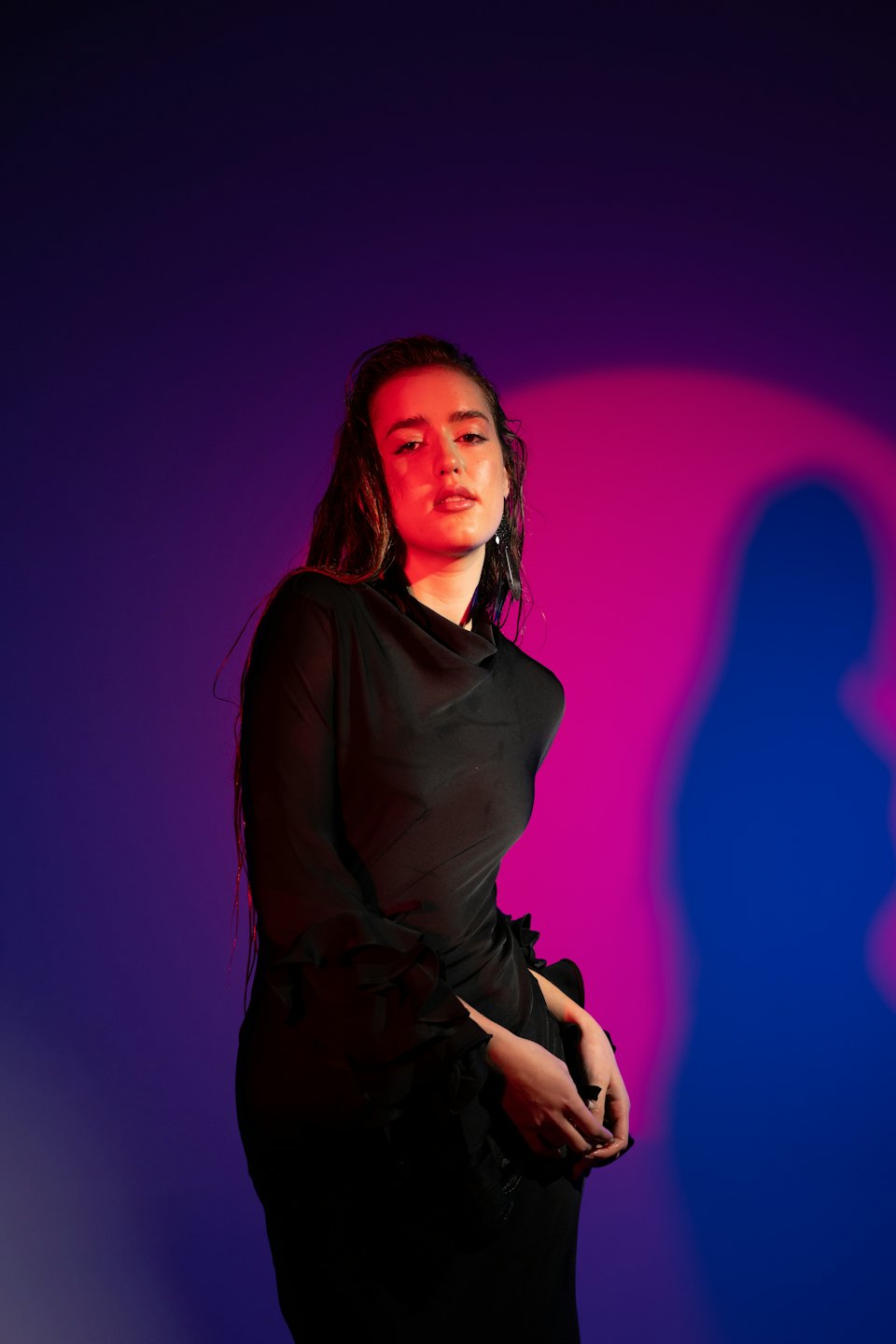 Donna in abito nero appoggiata a un muro.
