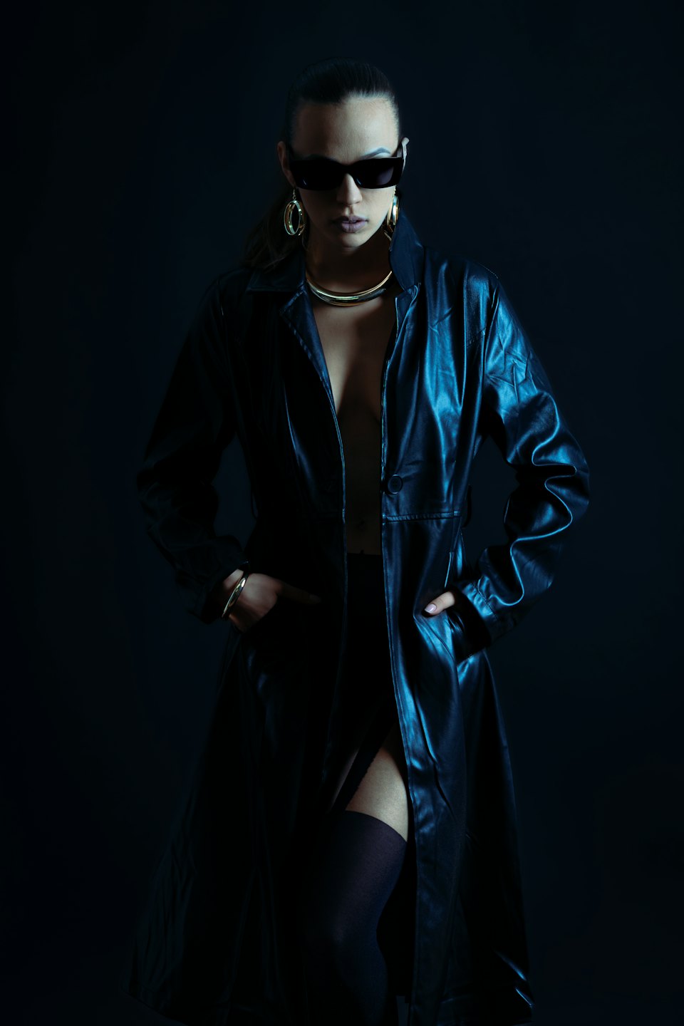 Donna con trench di pelle e gioielli d'oro in piedi ferma.
